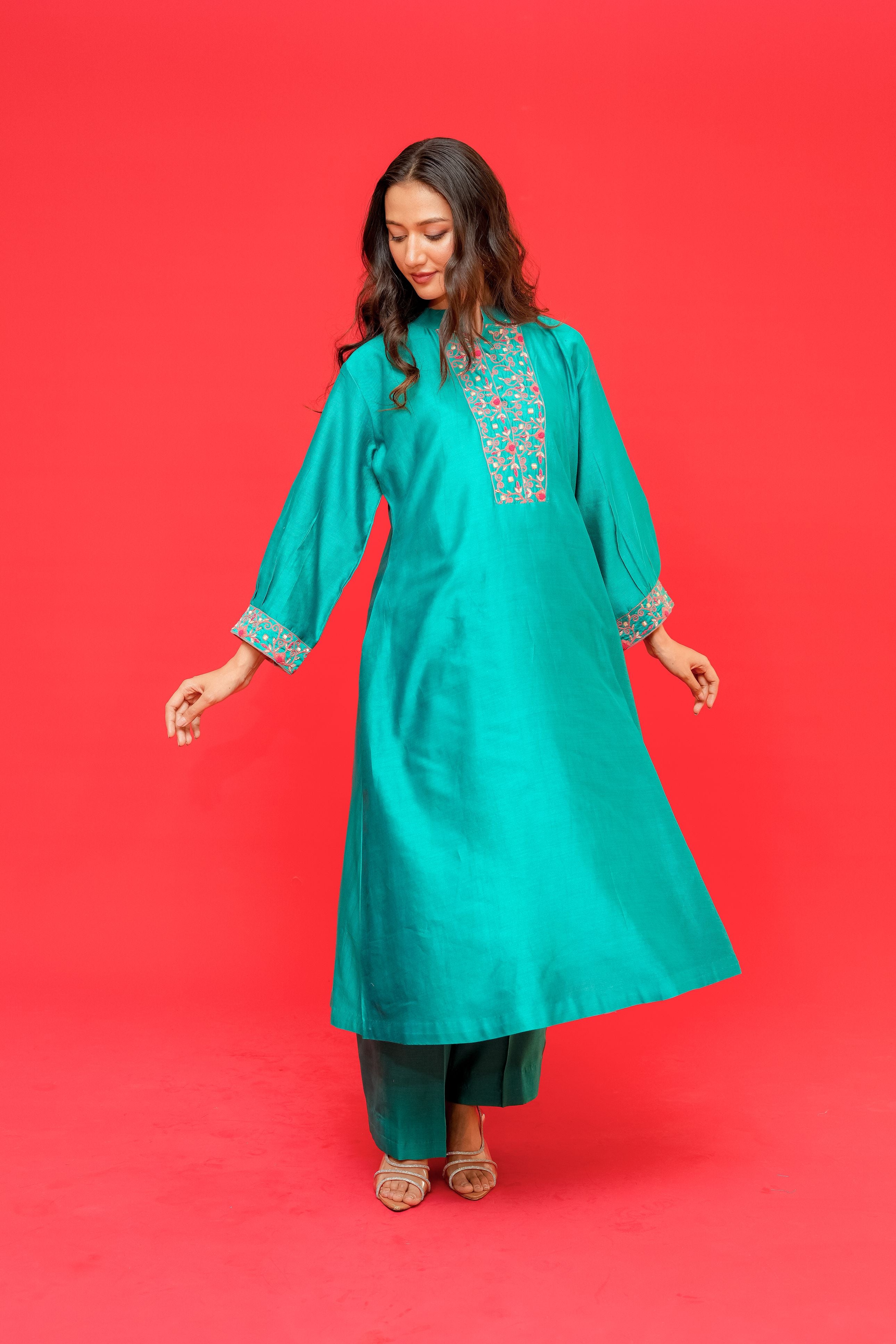 Woman wearing a teal embroidered kurta against a red background