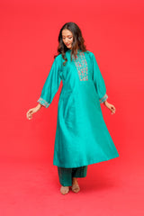 Woman wearing a teal embroidered kurta against a red background