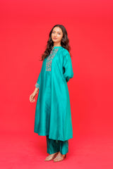 Woman wearing a teal traditional outfit with embroidery on a red background