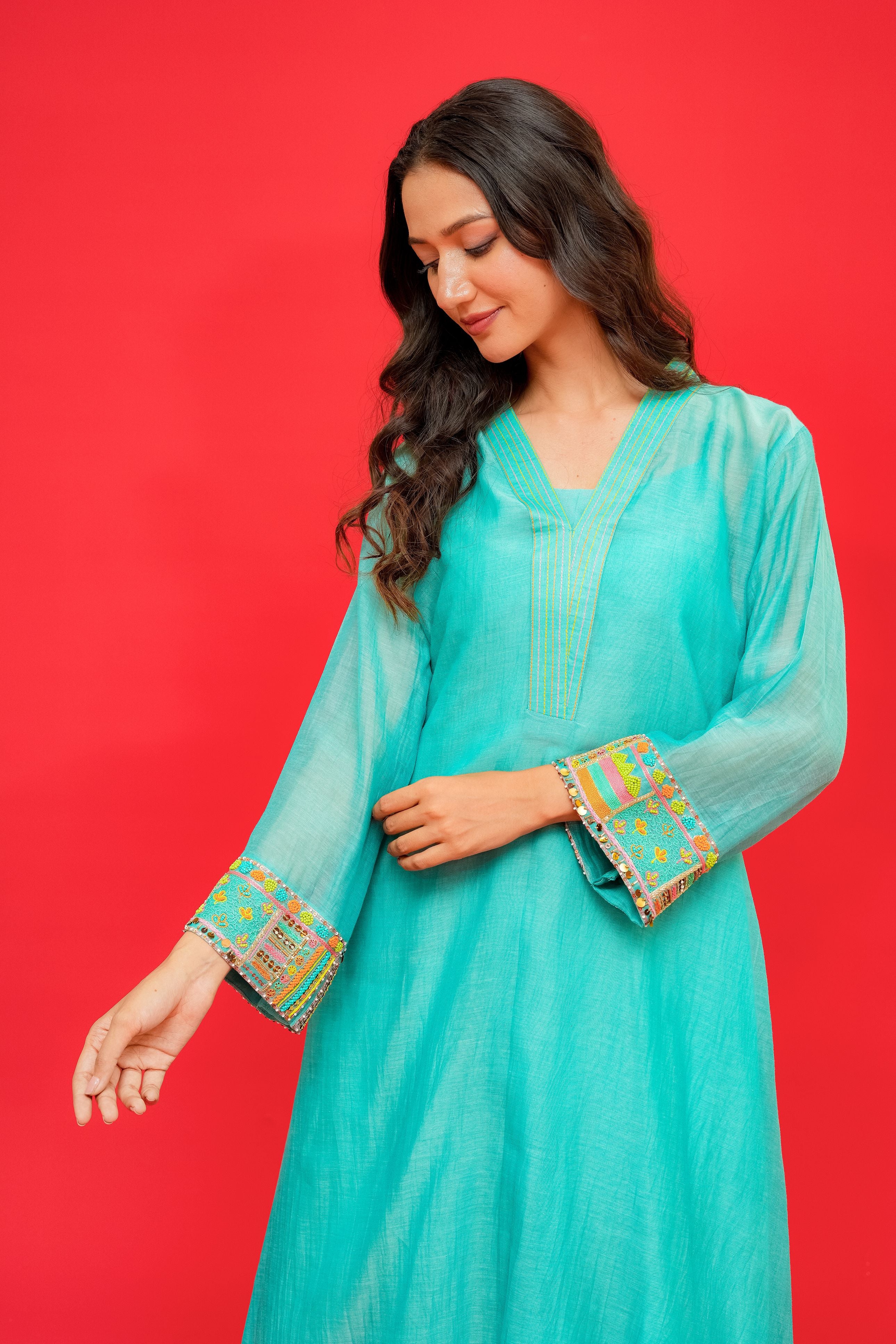 Woman wearing a turquoise traditional outfit with colorful embroidery on a red background
