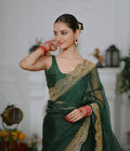 Woman in a green saree with gold embroidery posing indoors.