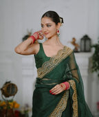 Woman in a green saree with gold embroidery posing indoors.