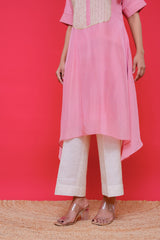 Person wearing a pink kurta with white pants against a red background