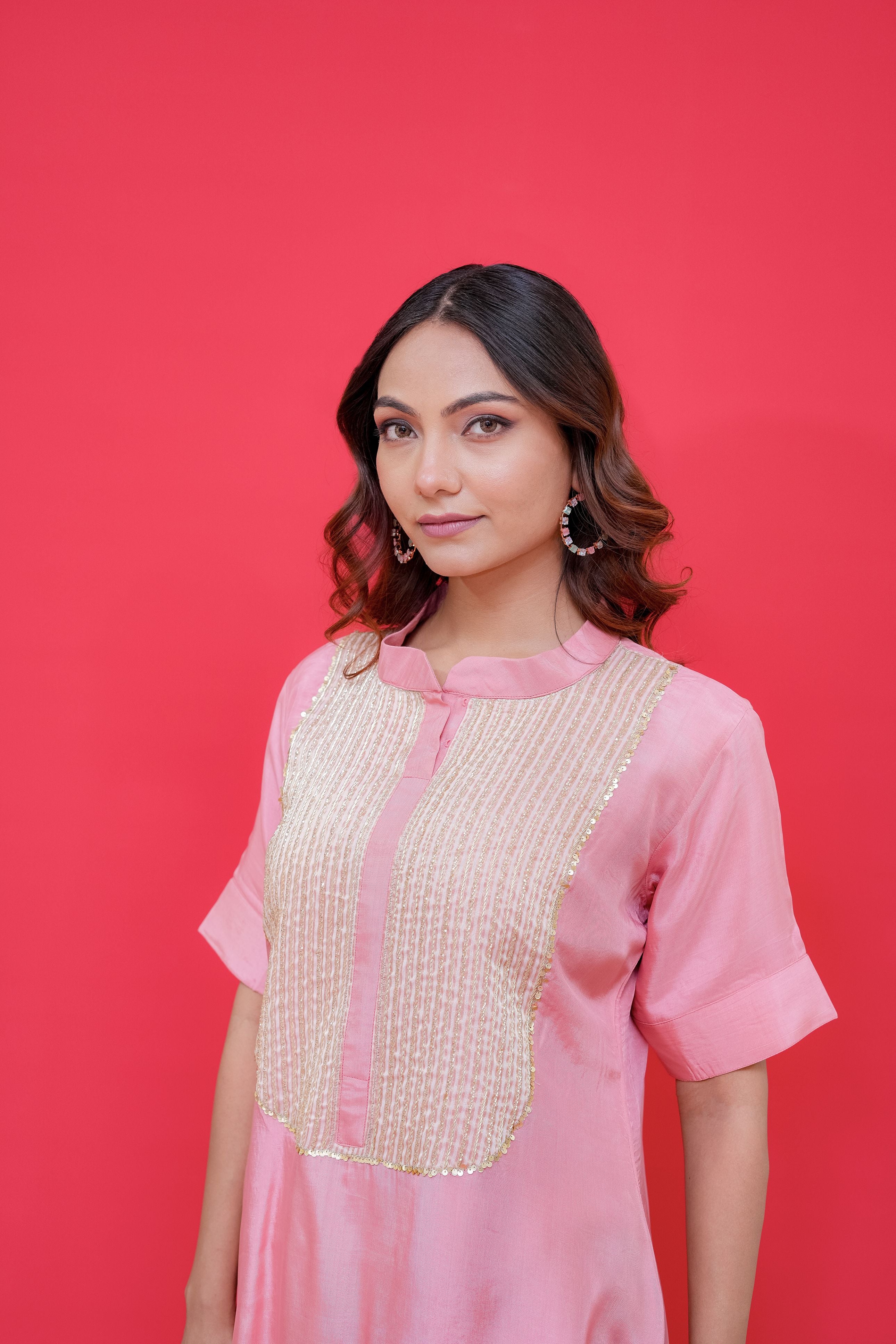 Woman wearing a pink traditional outfit with gold details against a red background