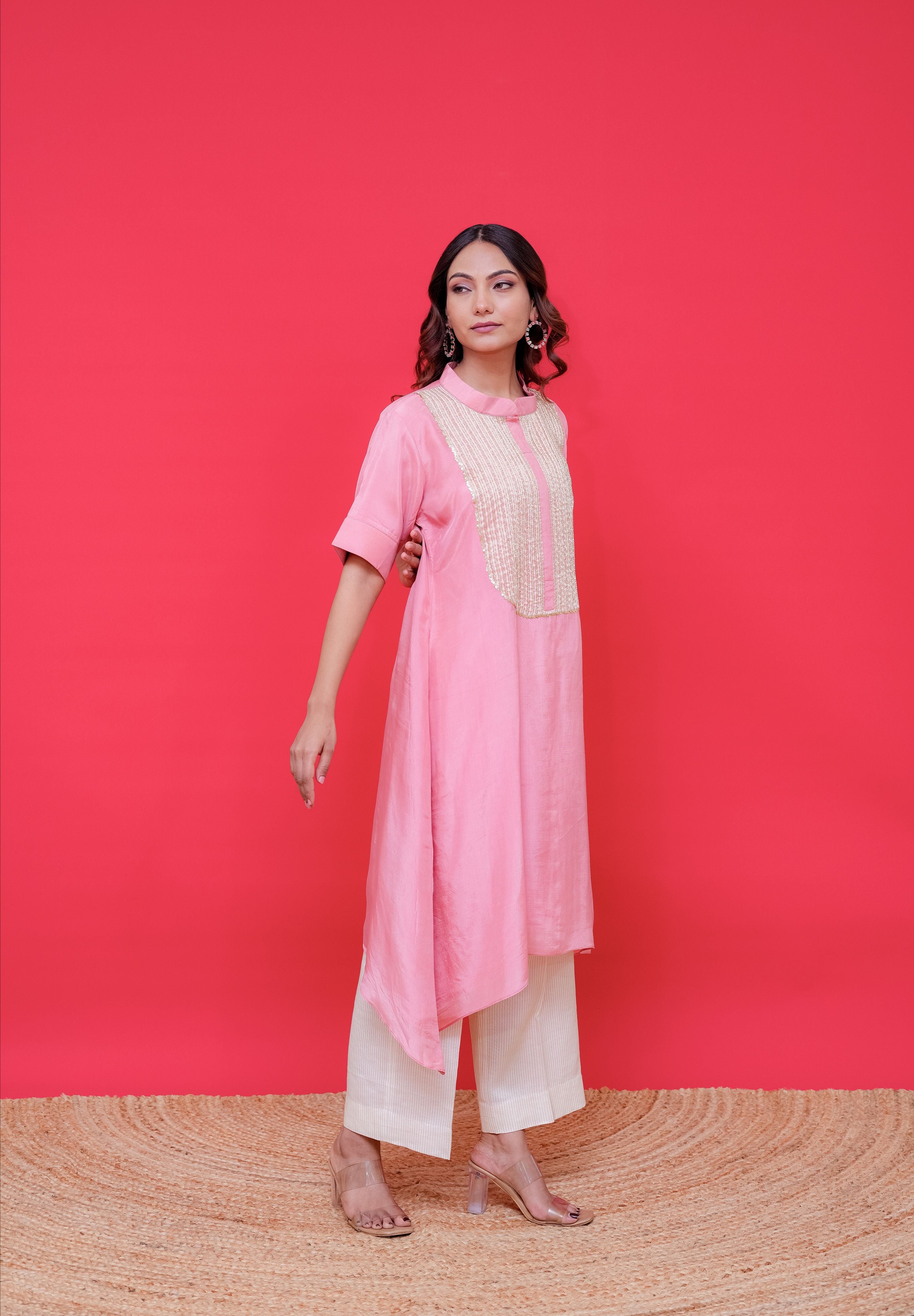 Woman wearing a pink kurta with white pants against a red background
